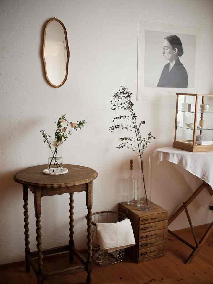 ブラウンの木目調と白い壁のナチュラルなアンティークリビング、ヴィンテージのテーブルと額縁が落ち着いた雰囲気を演出
