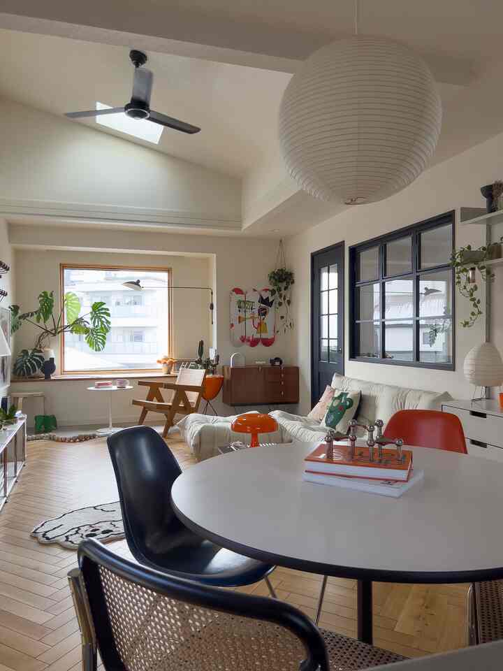 白とナチュラルトーンのリビング、ペンダントライトとオレンジのアクセントが配置された雰囲気のある空間