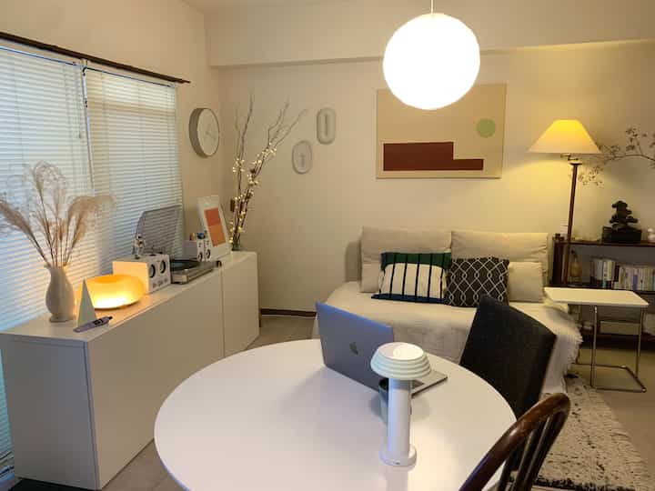 白とナチュラルカラーの1LDKリビング、ラウンドテーブルとソファ、ペンダントライトが配置された落ち着いたホームオフィス空間