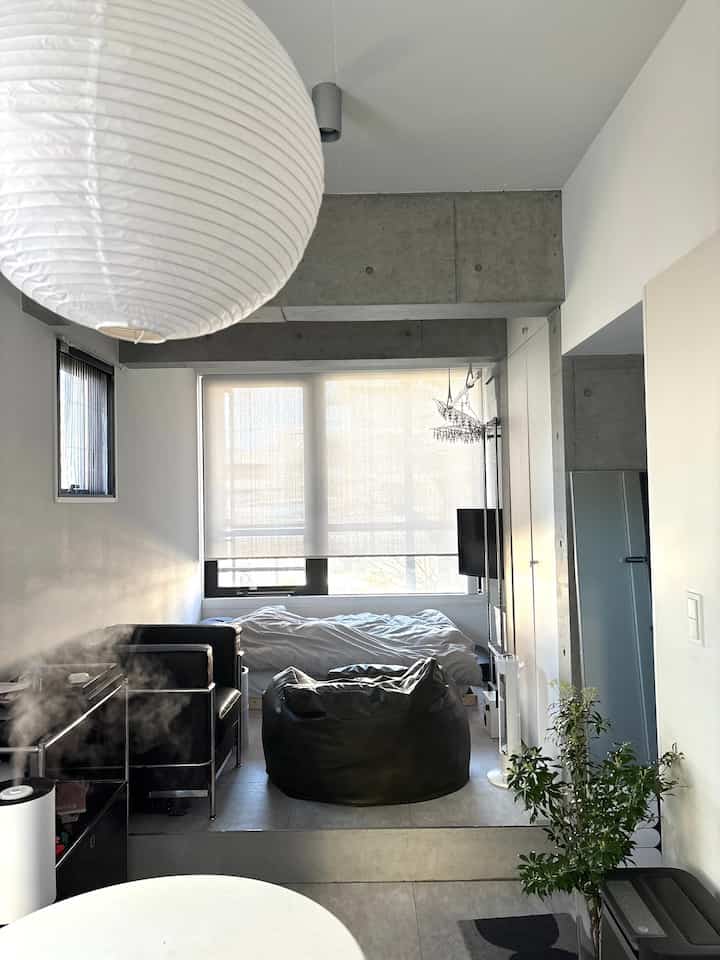 A compact bedroom with white and black tones, featuring a white paper lantern, black armchair, and bean bag, creating a natural modern vibe