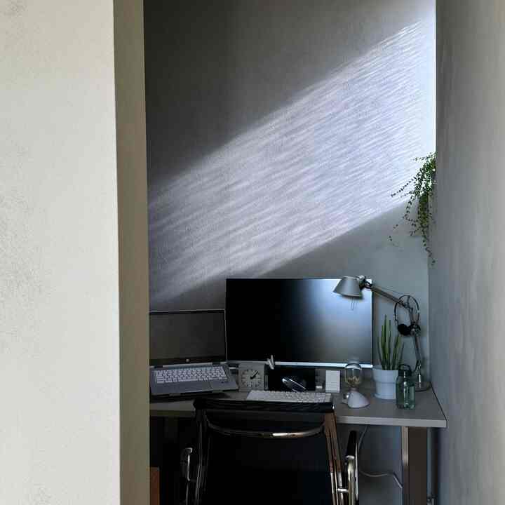 白とグレーのトーンの小さなホームオフィス空間、デスクとモニター、オフィスチェアが配置された清潔感のある作業スペース