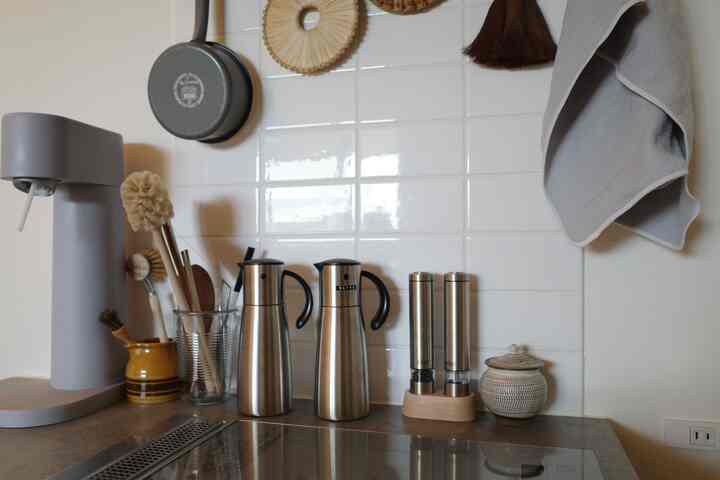 白いタイル壁とステンレスのオイルポット、塩胡椒ミルが配置された清潔感あるモダンなキッチン