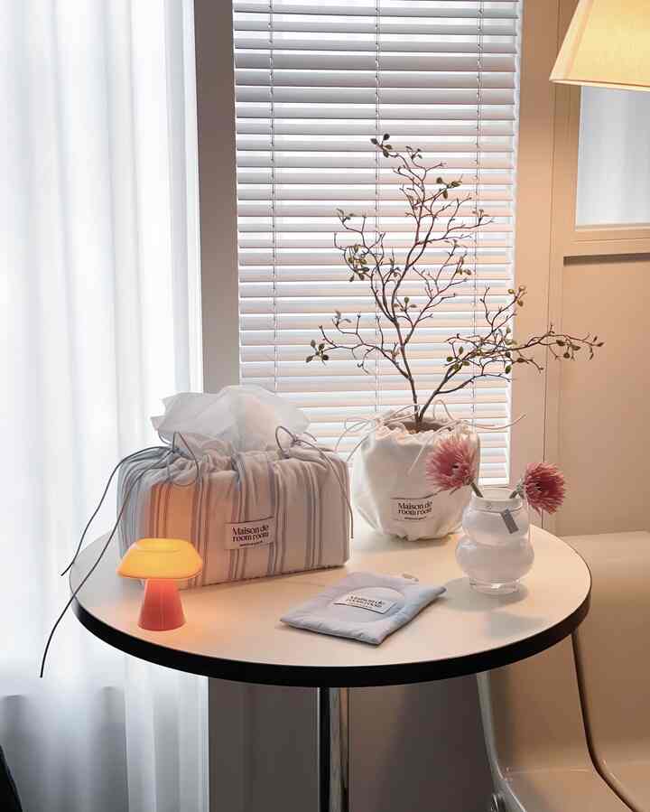 Minimal small room in white and beige tones with a round dining table featuring tissue boxes, a small lamp, and vases for a cozy cafe style ambiance
