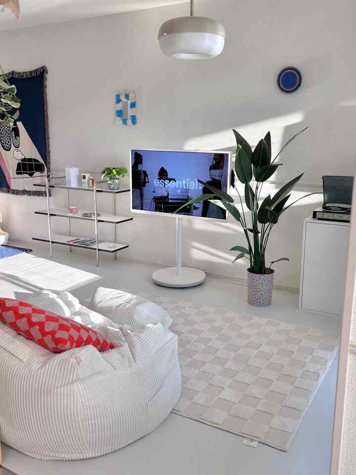 白とベージュのトーンの明るいモダンなリビング、中央にビーズクッションとテレビスタンド、大きな室内植物が配置された空間