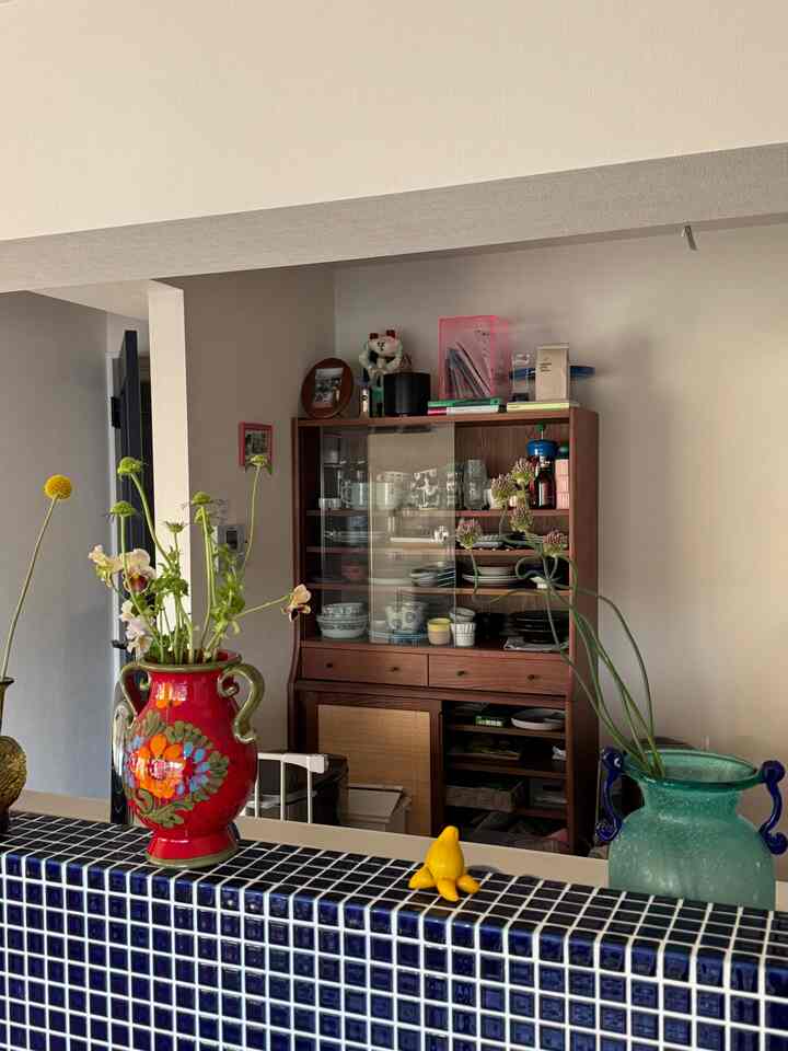 ウッドトーンとブルータイルが調和したキッチンスペース、花瓶と食器棚が配置された雰囲気のある空間