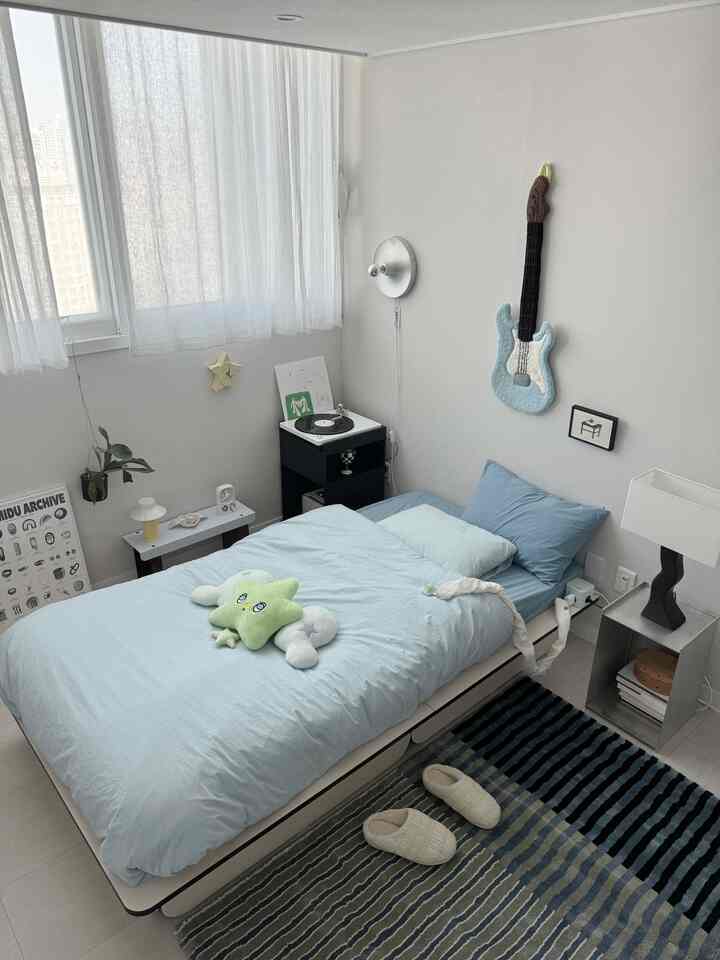 スカイブルートーンのワンルーム寝室、中央にシングルベッドとターンテーブルが配置された清潔感のあるモダンな空間