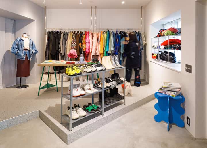 白い壁の玄関スペース、多彩な色の服が掛けられたオープンクローゼットと整頓された靴棚が配置された印象的な空間