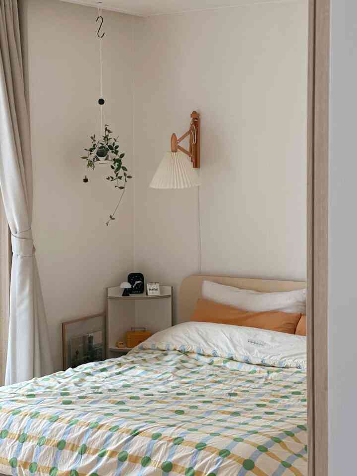 白とベージュのトーンの寝室、小さなコーナー棚とハンギングプラントが配置された、落ち着いた自然な雰囲気のあるインテリア