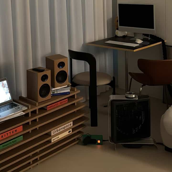 A wood tone and black-themed home office featuring desks, chairs, and speakers in a simple modern style