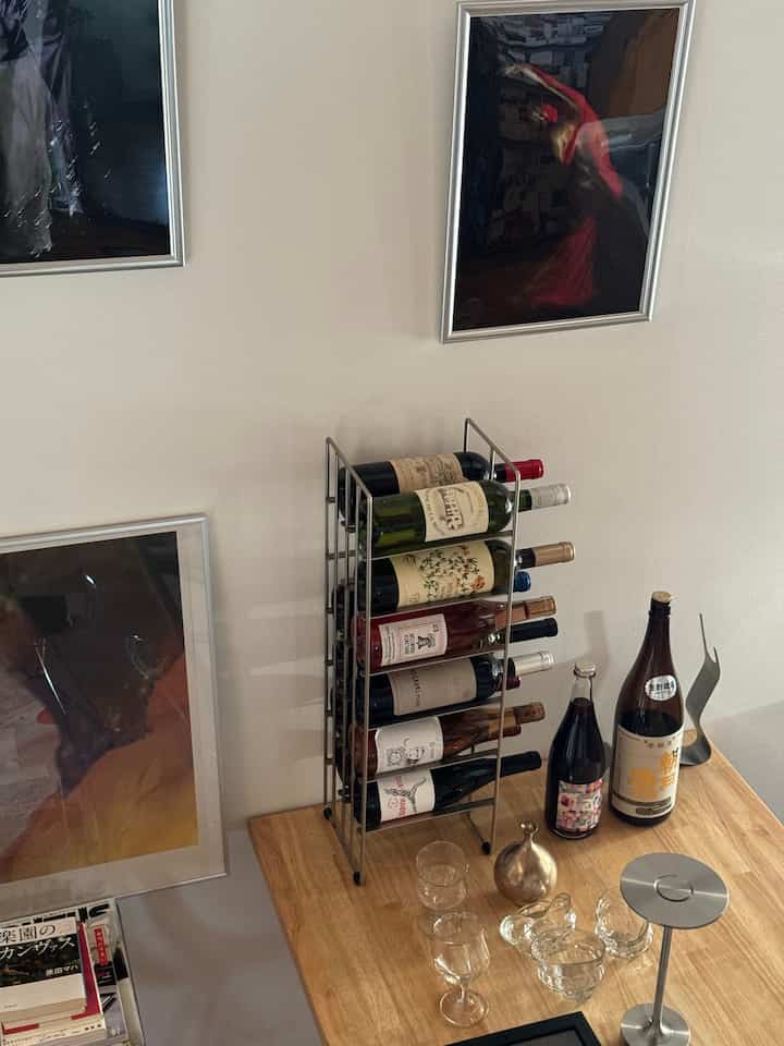 ナチュラルトーンの壁と木製テーブルにワインラックとワインボトル、グラスが配置された1LDKのリビングスペース