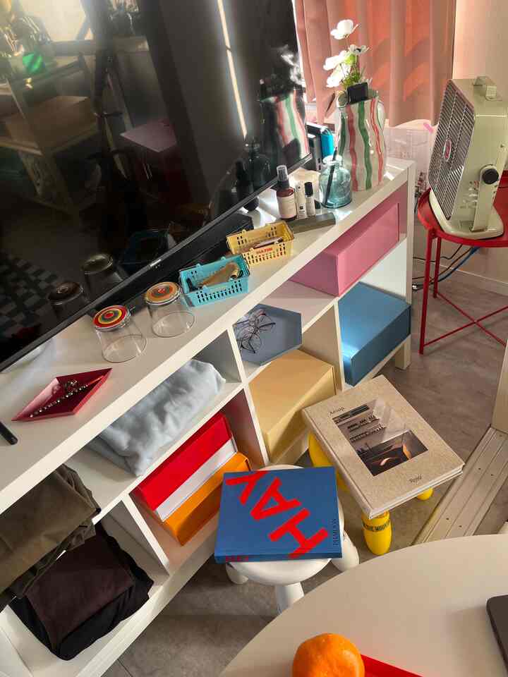 Living room in white and beige tones with colorful storage boxes, stools, and books arranged for a cozy atmosphere