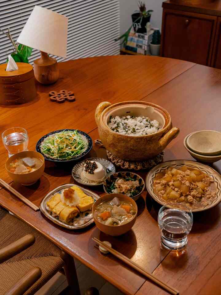 温かみのある木目調のダイニング、チーク材のテーブルに陶器の食器と日本風の炊飯器が配置された自然な雰囲気の空間
