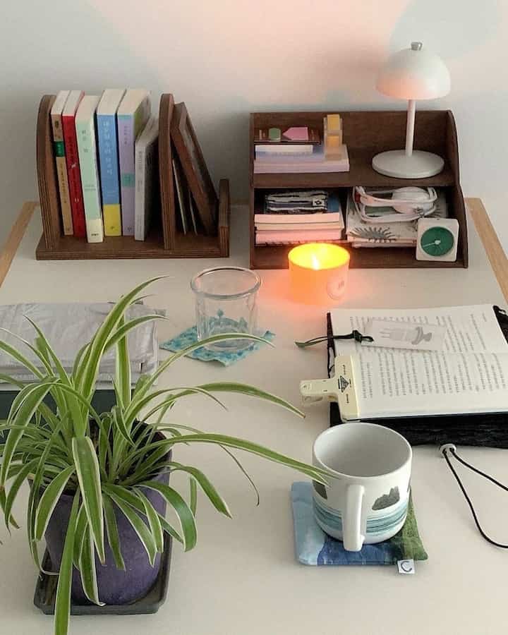 ホワイトトーンの小さなテーブル空間、本、植物、キャンドル、テーブルランプが配置された雰囲気のある読書と作業スペース