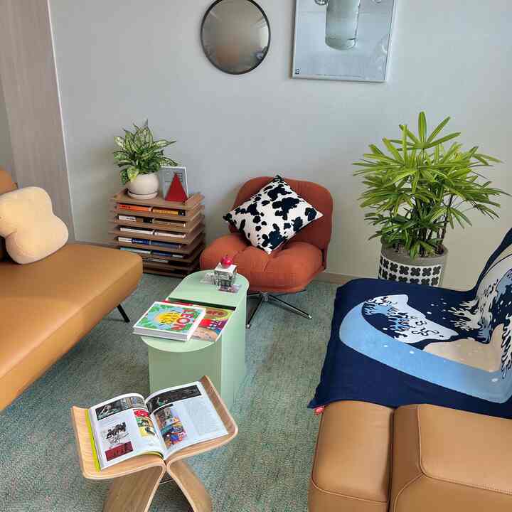 ベージュのソファとオレンジのアームチェアが配置されたナチュラルモダンなリビング、緑の植物とスツールが調和する空間