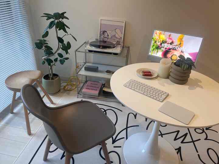 白とベージュのトーンのワンルームホームオフィス、丸テーブルとコンピューター、スツール、植物を配したシンプルなインテリア