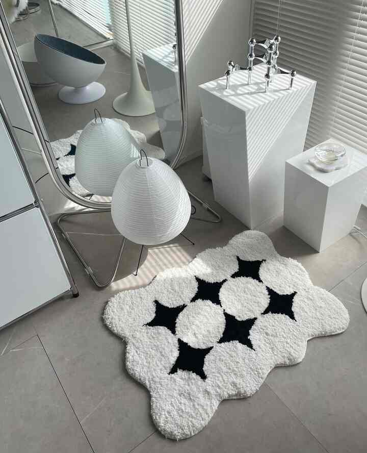 モダンな白色調のワンルーム、黒のパターンラグとシルバースチールミラーが配置された印象的なインテリア