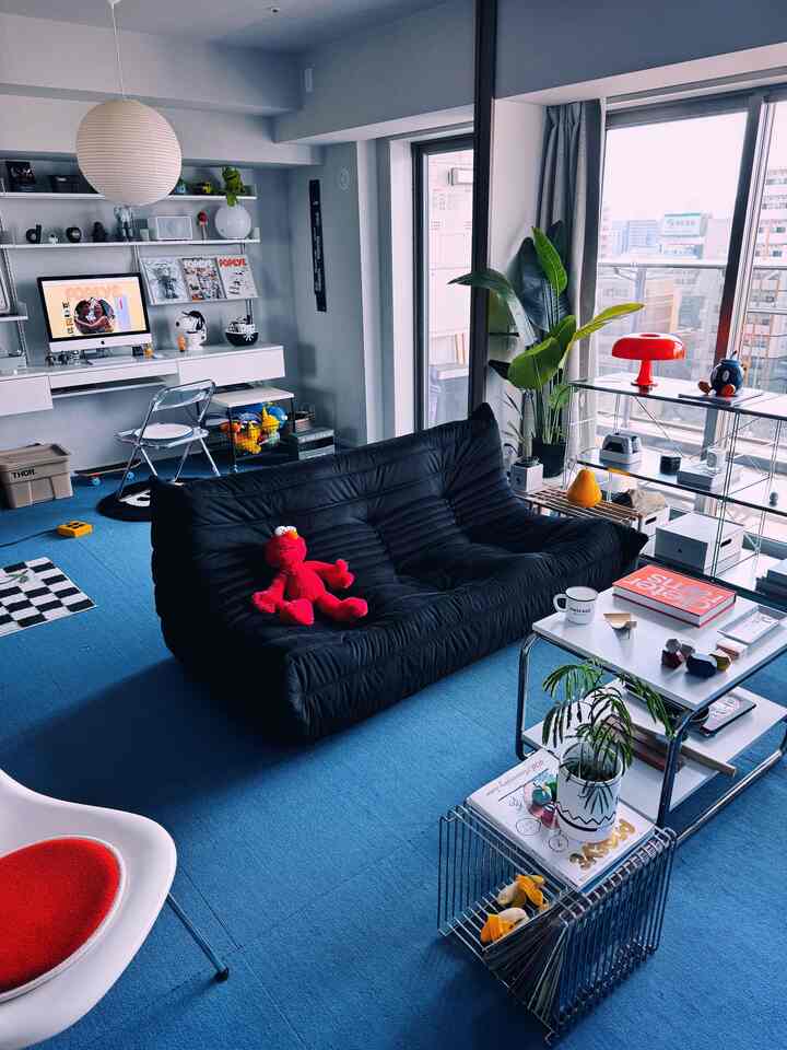 ブルーカーペットと黒いソファが配置されたリビングルーム、ホームオフィスの要素を持つモダンな都市型アパート空間