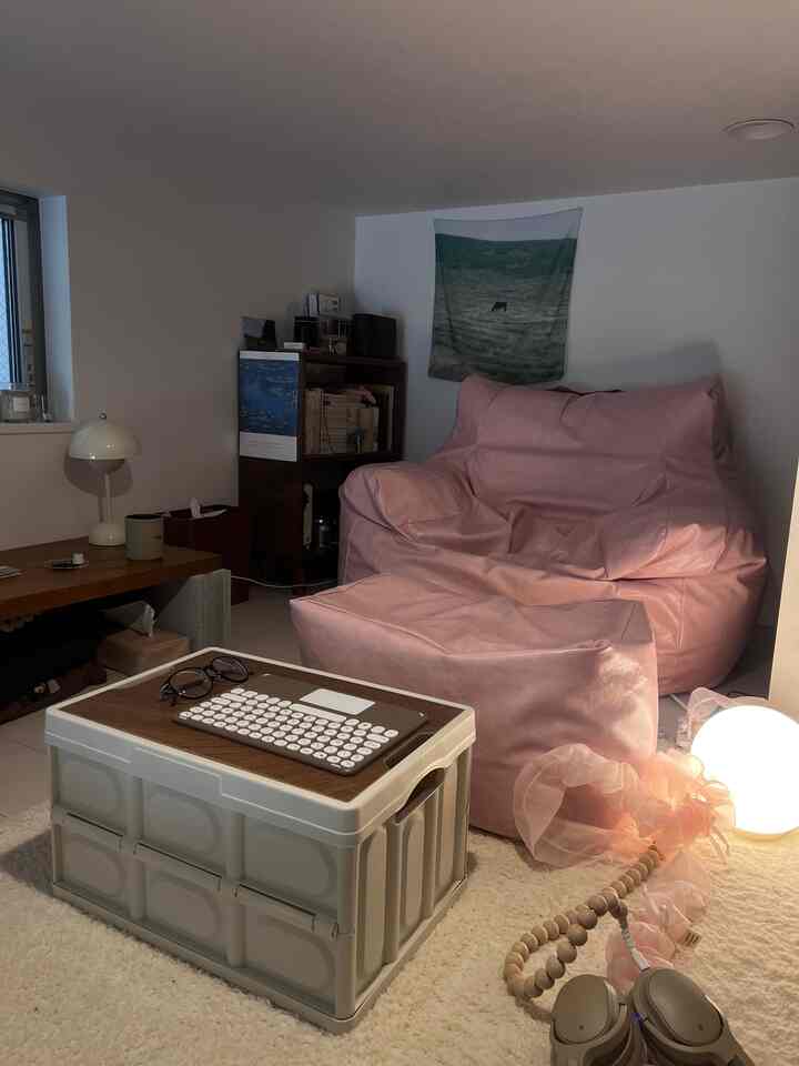 柔らかなピンクのビーズクッションとナチュラルカラーの収納ボックスが配置された、居心地の良いコンパクトなワンルームのリビング