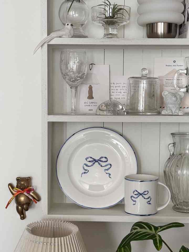 Kitchen dish cabinet in white and transparent glass tones featuring plate and mug with blue ribbon design in a simple setting