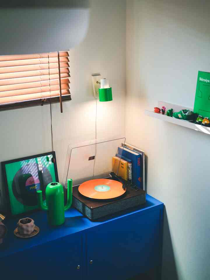 青いキャビネットの上にオレンジ色のレコードと緑色の小物が配置された雰囲気あるコーナー