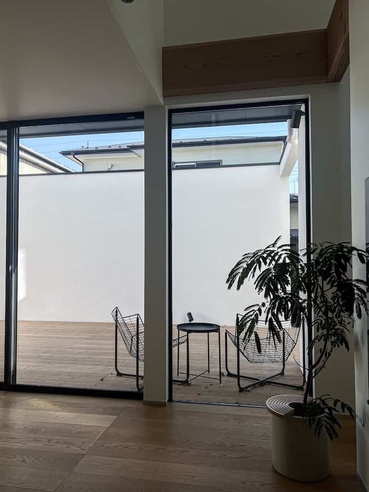 Wood tone floor and white walls define a balcony with black metal chairs, side table, and large plant creating a minimal modern vibe