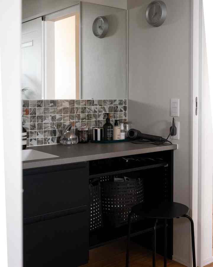 ニュートラルトーンのバスルーム、鏡と洗面台、黒い収納バスケットとスツールが配置されたモダンなインテリア