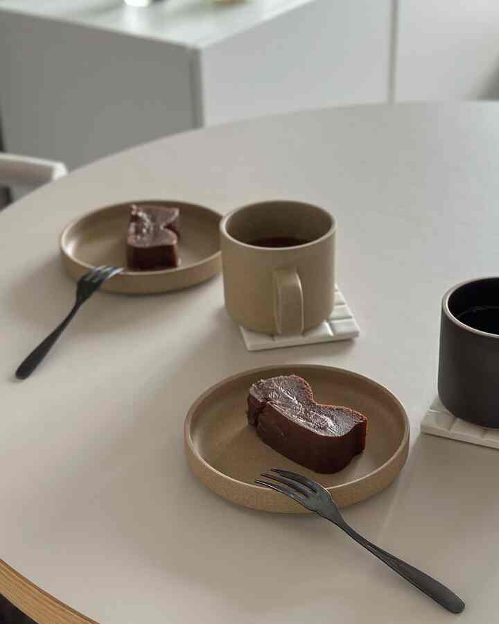 Beige and dark brown toned dining room with round table featuring mugs and cake in a simple home cafe setting