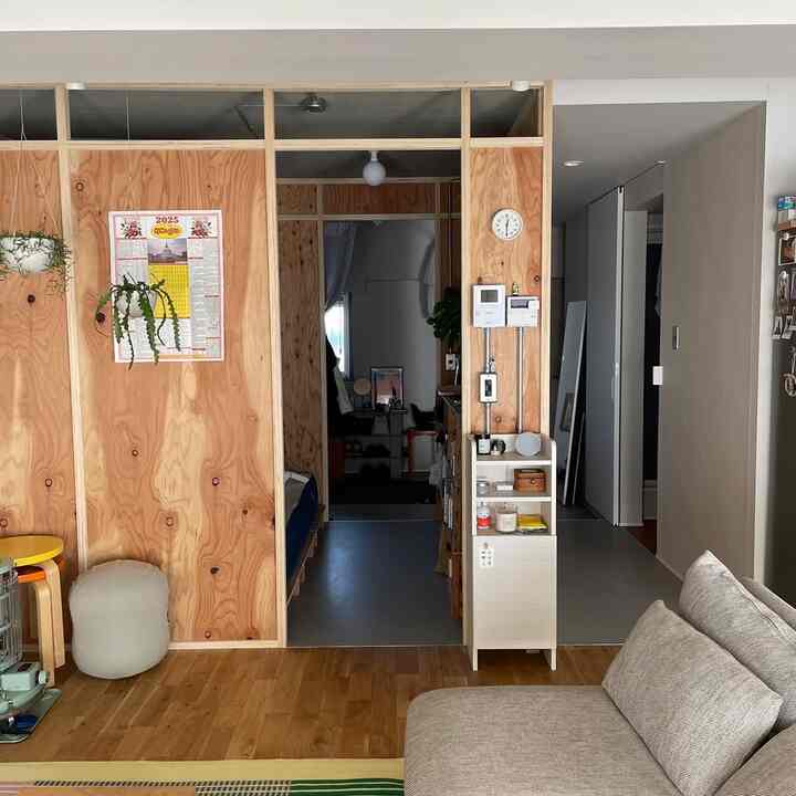 ナチュラルカラーと木目調の調和が美しいリビング、ベージュのソファと構造用合板の壁が印象的なコンパクトな空間