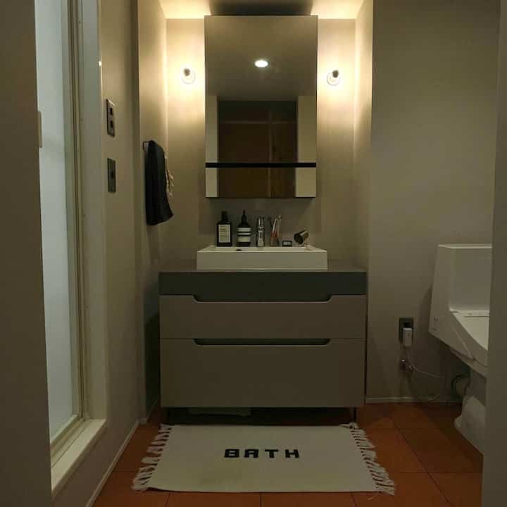 温かみのあるオレンジ色のテラコッタ風フロアタイルとミニマルな化粧台が配置された雰囲気のあるバスルーム