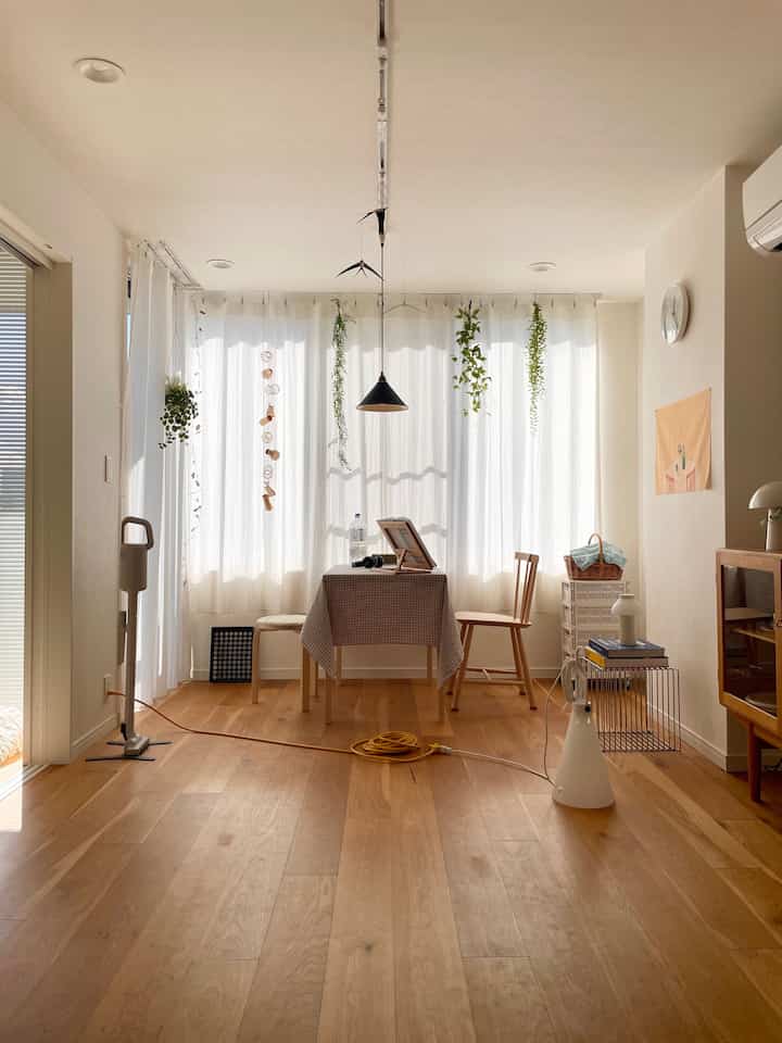 明るいホワイトの色調とブラウンの無垢材フローリングが特徴のコンパクトなダイニング、チェック柄のテーブルクロスと木製の椅子が配置された自然な雰囲気のインテリア