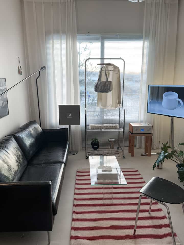 Modern living room with white background, black sofa, and silver mobile clothes rack