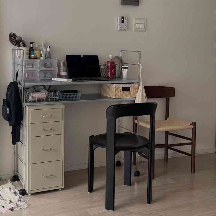 ベージュのチェストとメタルシェルフがあるコンパクトなモダンホームオフィス、黒いデスクチェアと木製の椅子が配置された清潔感のある作業空間
