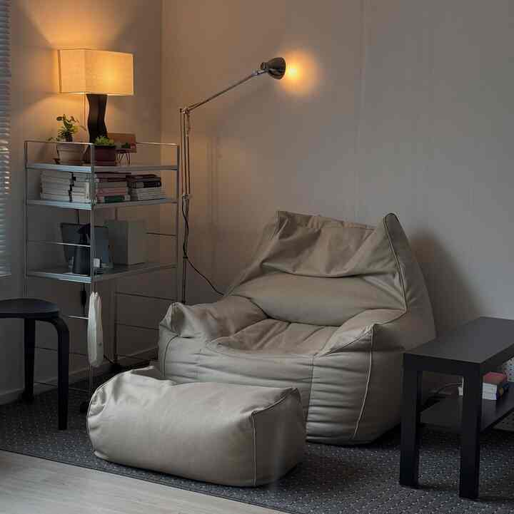 ベージュと黒を基調とした一人暮らしの空間、ビーズクッションソファとフロアスタンドランプが温かみのある読書の雰囲気を演出するアットホームなインテリア