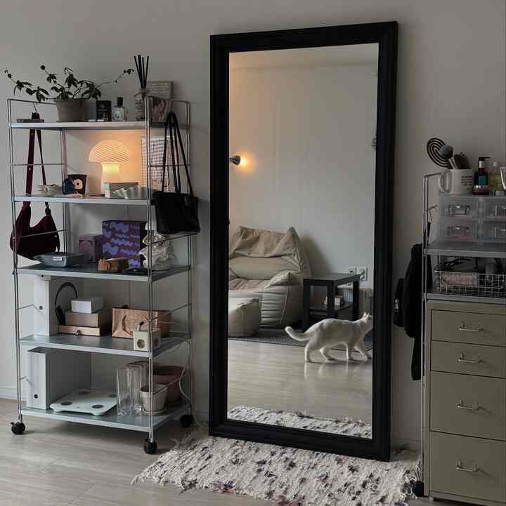 落ち着いたナチュラルトーンのリビング、大きな黒い鏡とメタルシェルフ、白い猫がいるシンプルな空間