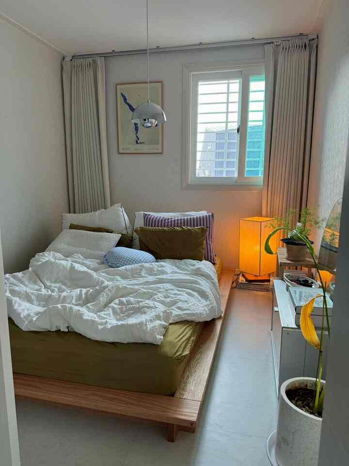 ホワイトと木目調が調和したコンパクトな寝室、シンプルなベッドと植物、温かみのある照明が居心地の良い雰囲気を演出する空間