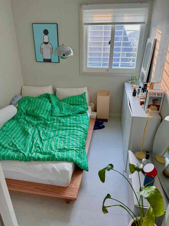 ナチュラルトーンの小さな寝室、木製ベッドと白い家具が調和し、グリーンの寝具がアクセントの温かみのあるインテリア