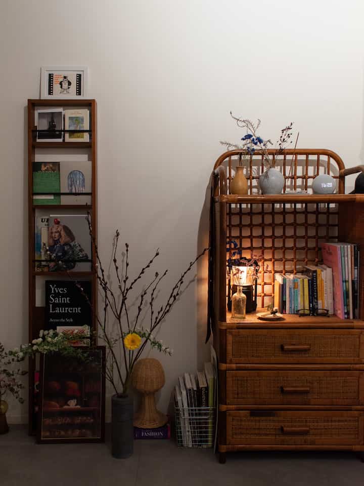 ナチュラルな色調のワンルーム読書スペース、木製の本棚とフロアランプ、花瓶と植物が配置された雰囲気のあるインテリア