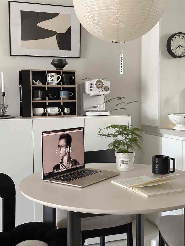 白い壁と木目調が調和したダイニングルーム、円形テーブルにはノートパソコンやコーヒーマシンが置かれた雰囲気のあるおうちカフェ空間