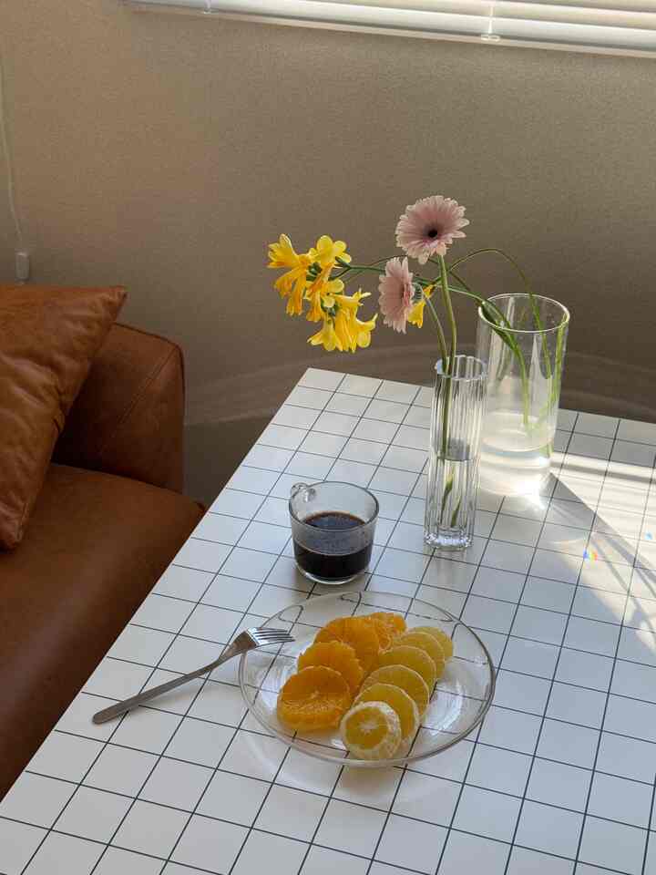 ナチュラルなベージュの壁と白いタイルのテーブル、ブラウンのソファと花瓶が配置された居心地の良い二人暮らしのおうちカフェ空間