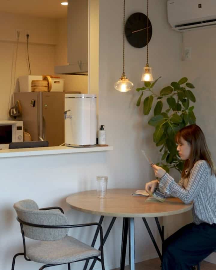 Natural wood round dining table with black metal legs in a white-walled dining room, featuring pendant lights and seating for two