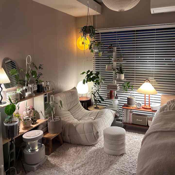 Soft white and beige toned studio living room featuring a plush natural modern sofa and numerous indoor plants creating a cozy atmosphere