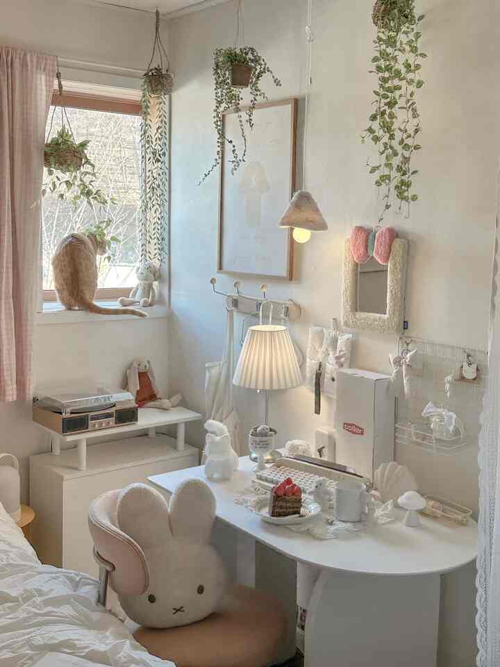 白を基調としたワンルームの書斎空間、かわいいぬいぐるみ椅子と吊り植物、照明が配置され、窓辺には猫が座る雰囲気のあるインテリア
