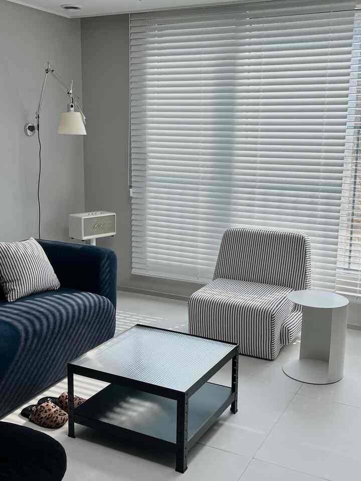 A modern living room in white and black tones featuring a navy sofa and white blinds creating a clean and balanced atmosphere