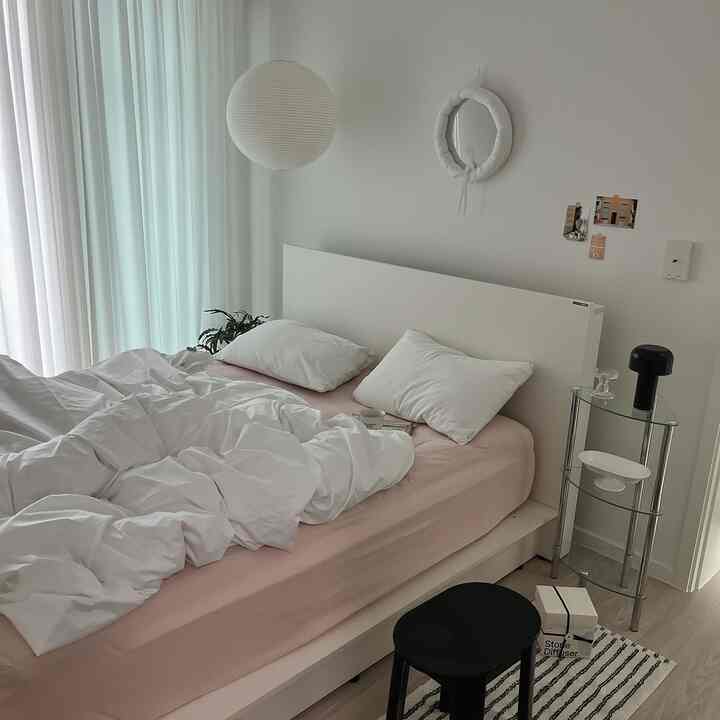 White and soft pink bedroom featuring clean bedding with black stool and lighting creating a cozy atmosphere