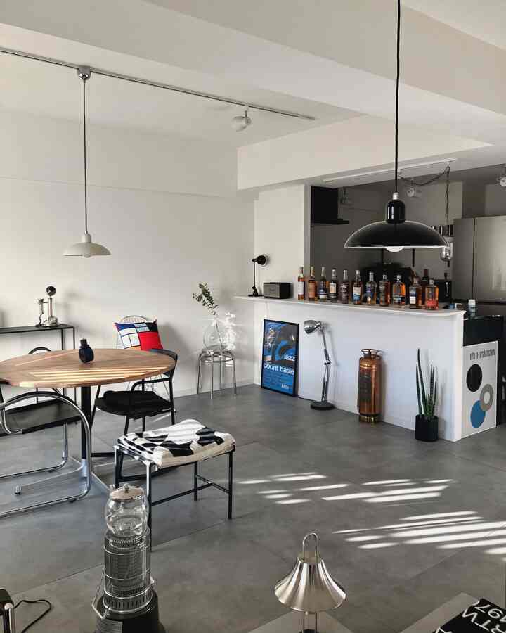 白とグレーの色調のリビング兼ホームバー空間、丸いダイニングテーブルと金属製の椅子が配置されたモダンでインダストリアルなインテリア