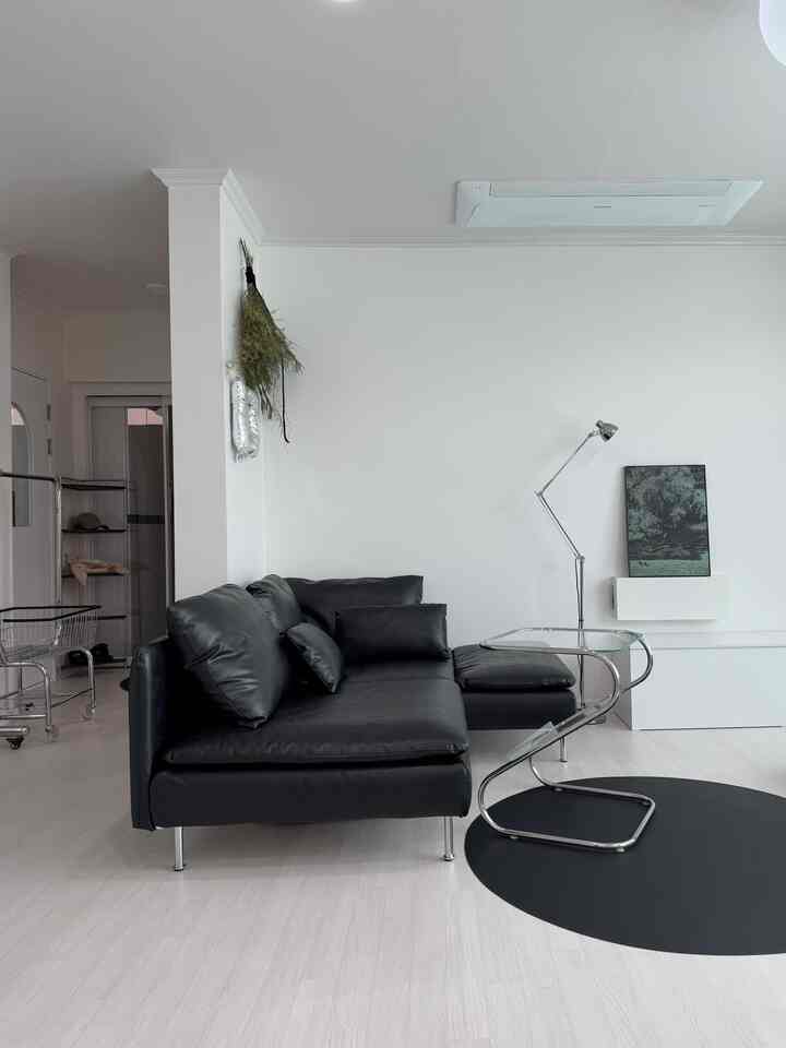白い壁と床に黒のコーナーソファとシルバーの金属製家具が配置されたミニマルなリビング