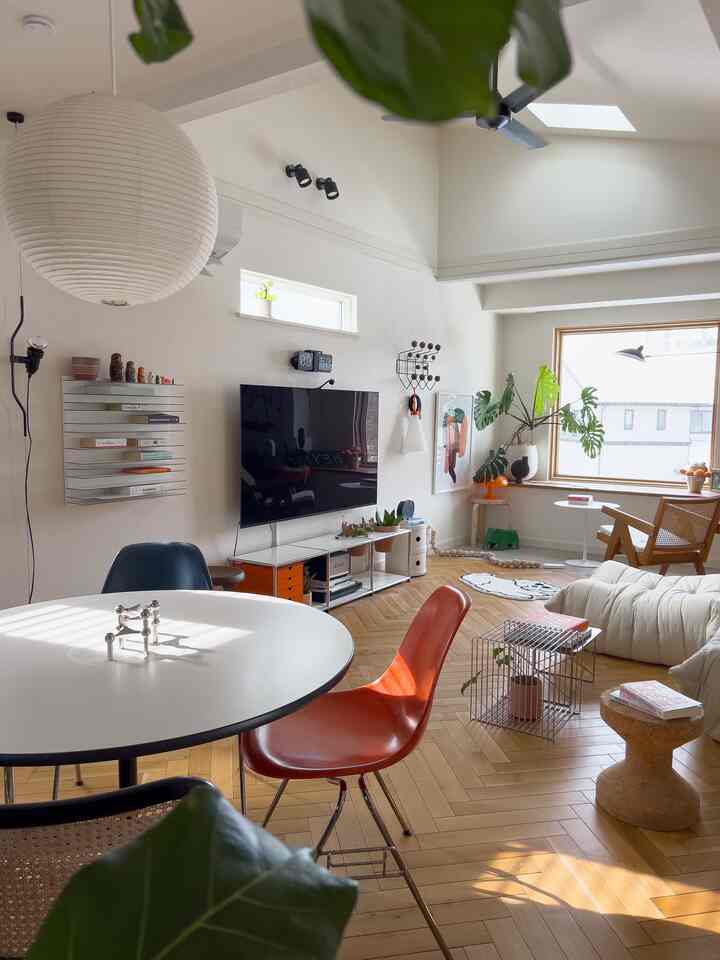Bright living room with white walls, round dining table, brown herringbone wood floor, mid-century modern chairs and sofa arranged cozy