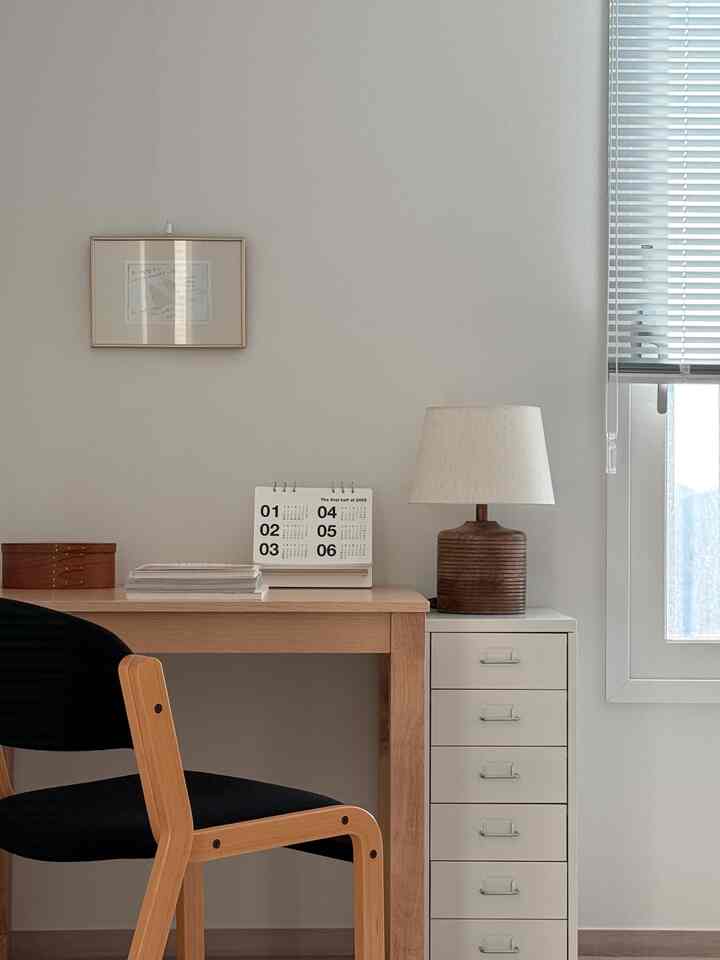 ナチュラルな色調のホームオフィス、木製デスクと白い引き出し、シンプルな照明と額縁のある清潔感のある空間