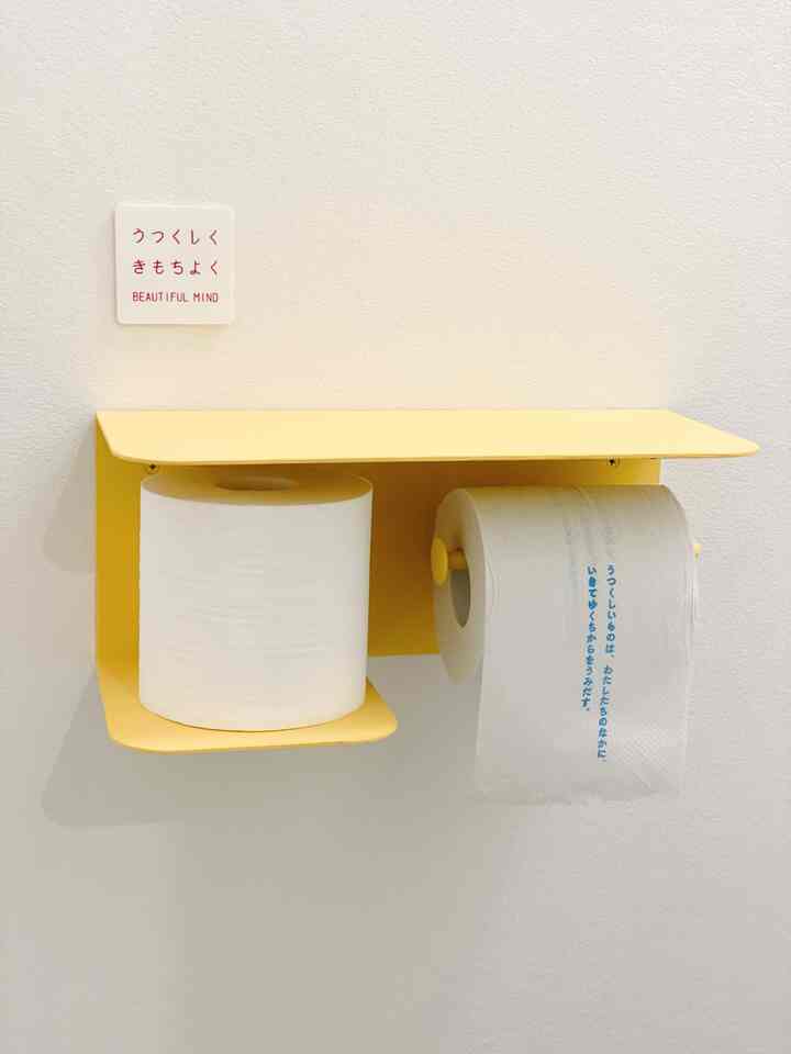 Yellow wall-mounted toilet paper holder with two white toilet paper rolls on a clean white wall, simple bathroom setup