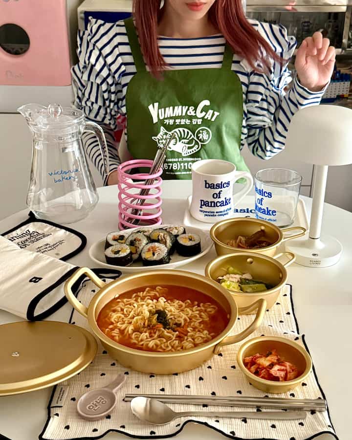 Warm kitchen dining table with gold-colored pot, various tableware, and food in a cozy home cafe atmosphere